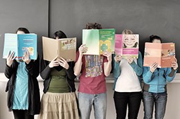 Schülerinnen stehen in einer Reihe und halten sich Bücher vors Gesicht