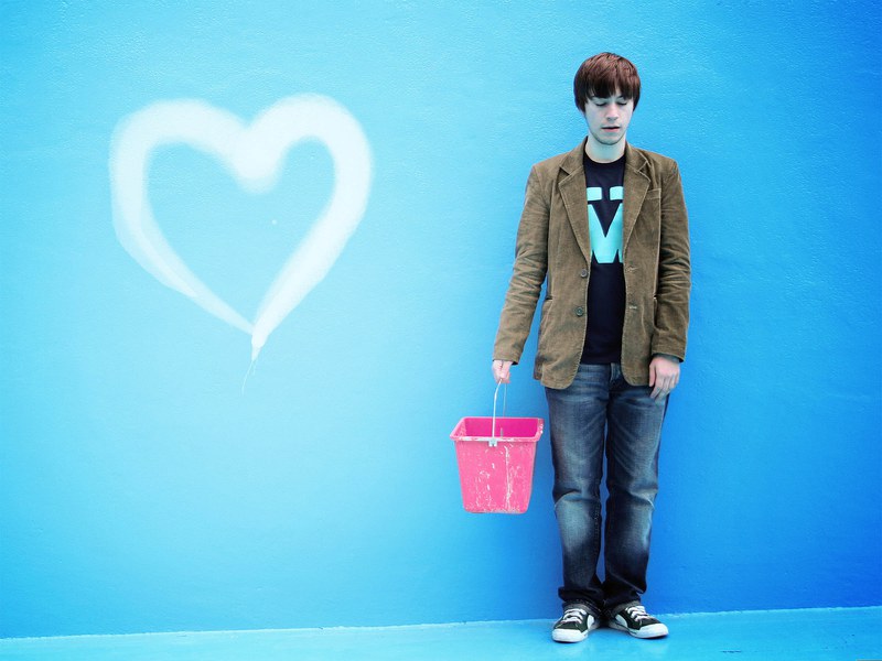 Mann mit rosarotem Farbeimer vor blauer Wand